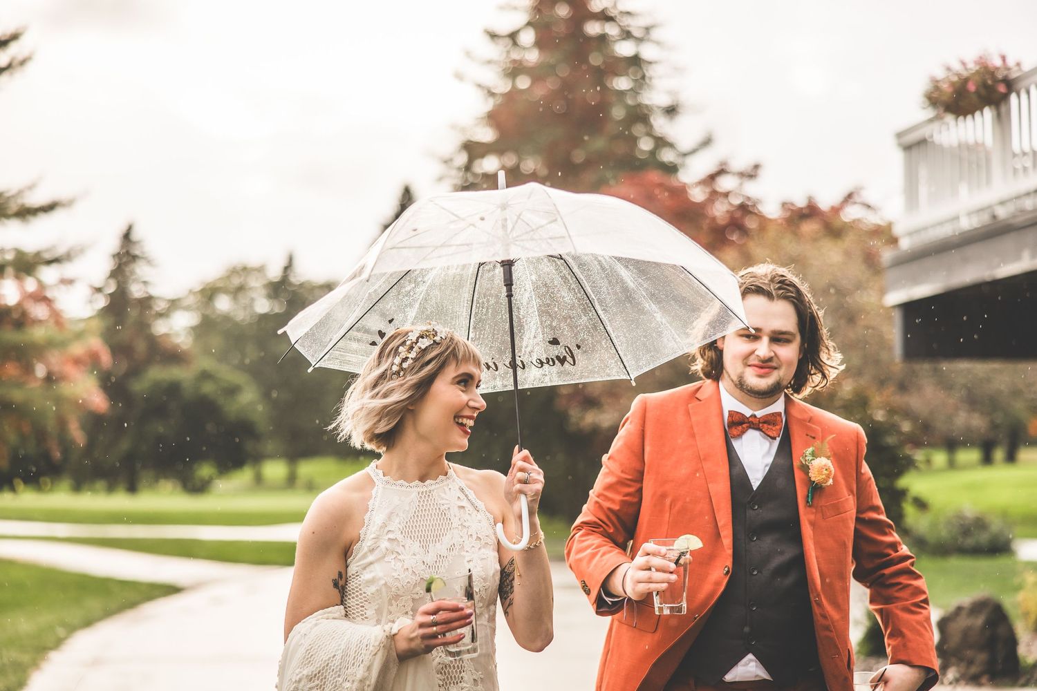 Romantic rainy day wedding photos with couple sharing clear umbrella on golf course path.