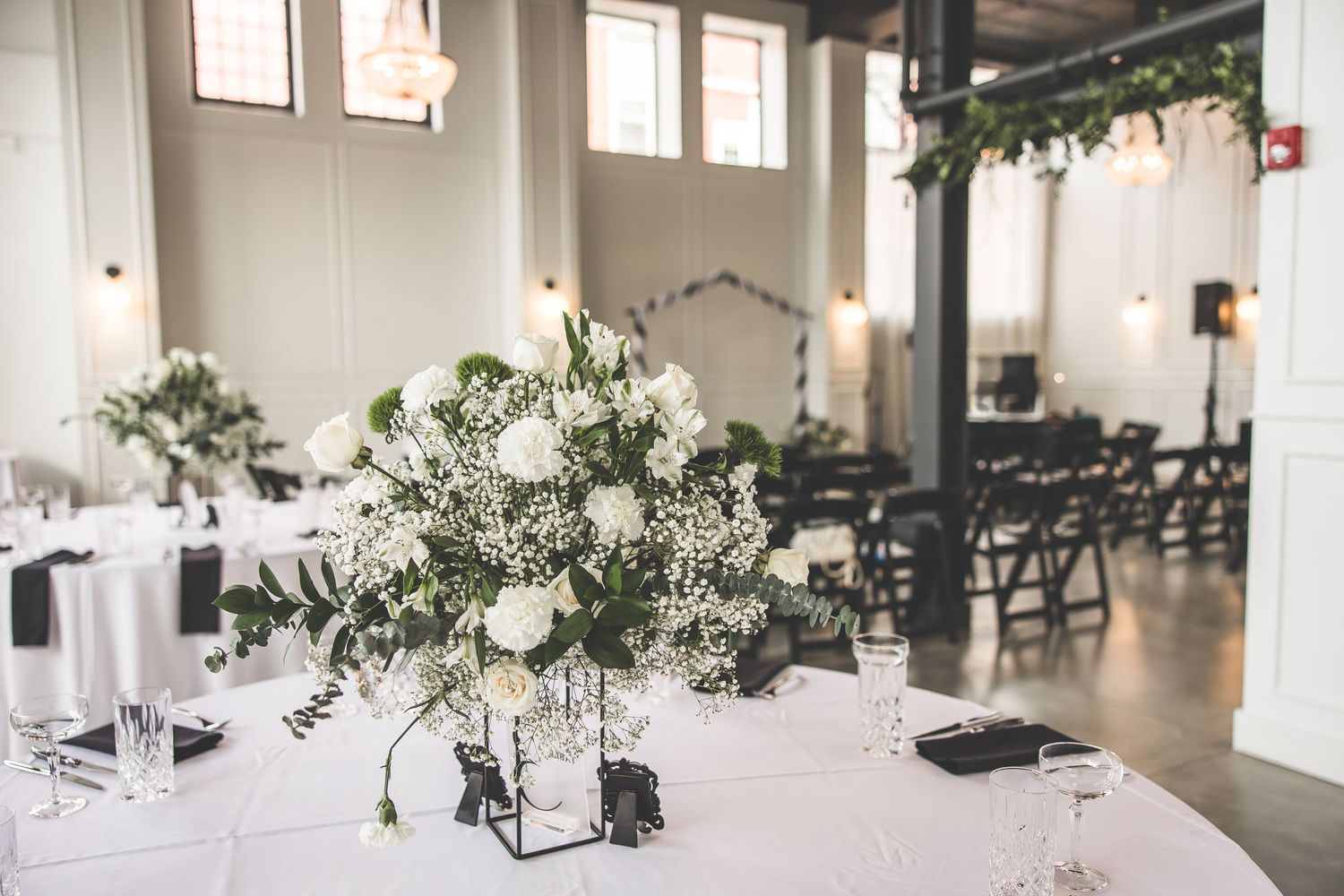 Elegant wedding reception space with greenery accents and natural lighting from tall windows.