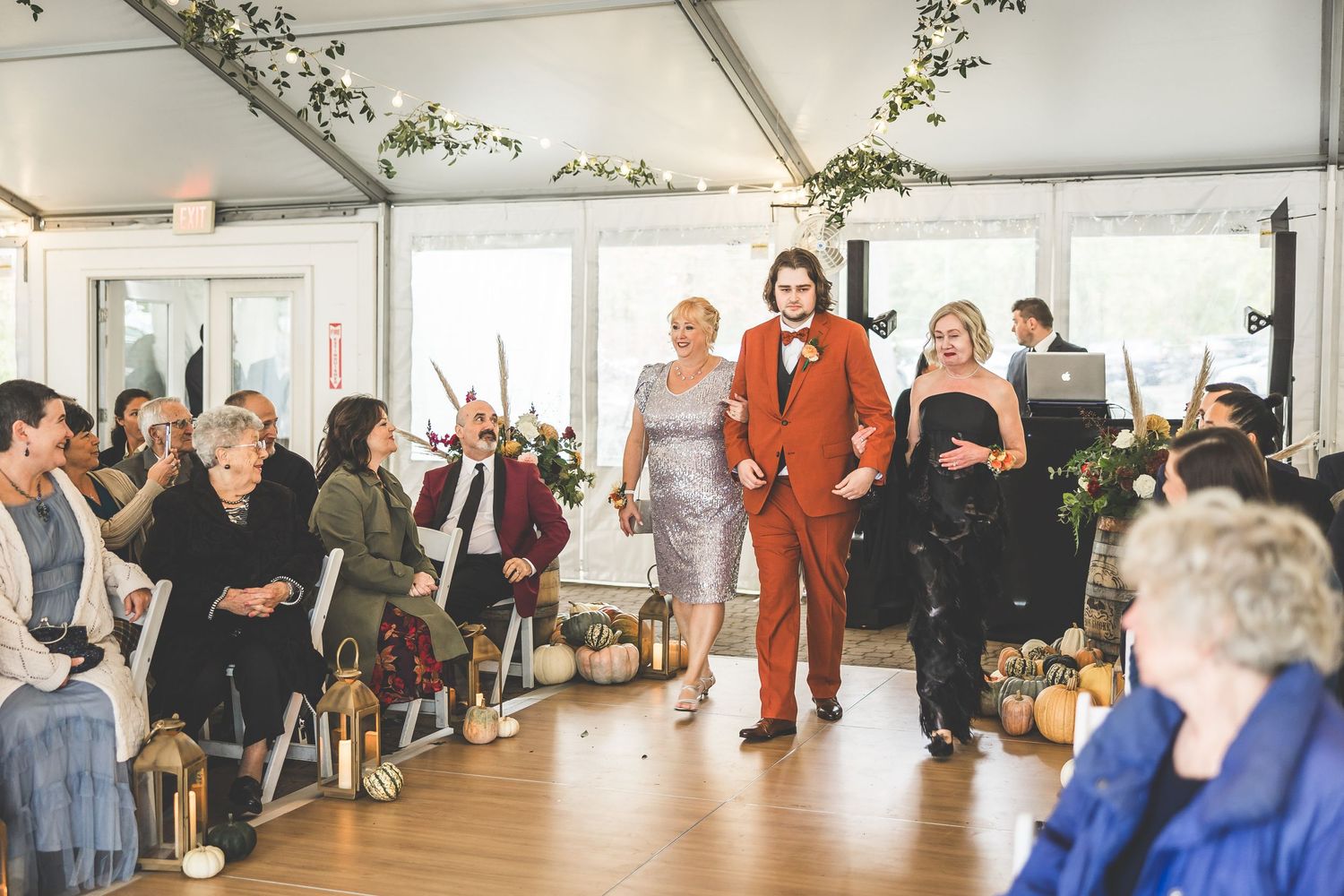 Wedding guests gather in a bright indoor reception space with white walls and string lights.