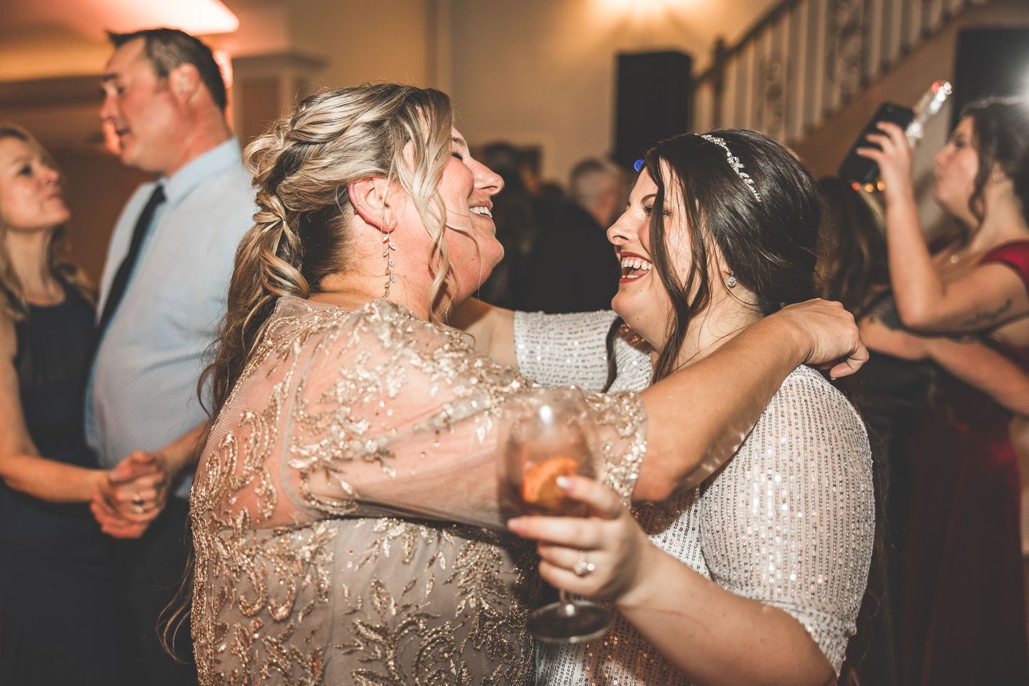 Wedding reception guests dancing and celebrating on a dance floor with colorful lighting effects.