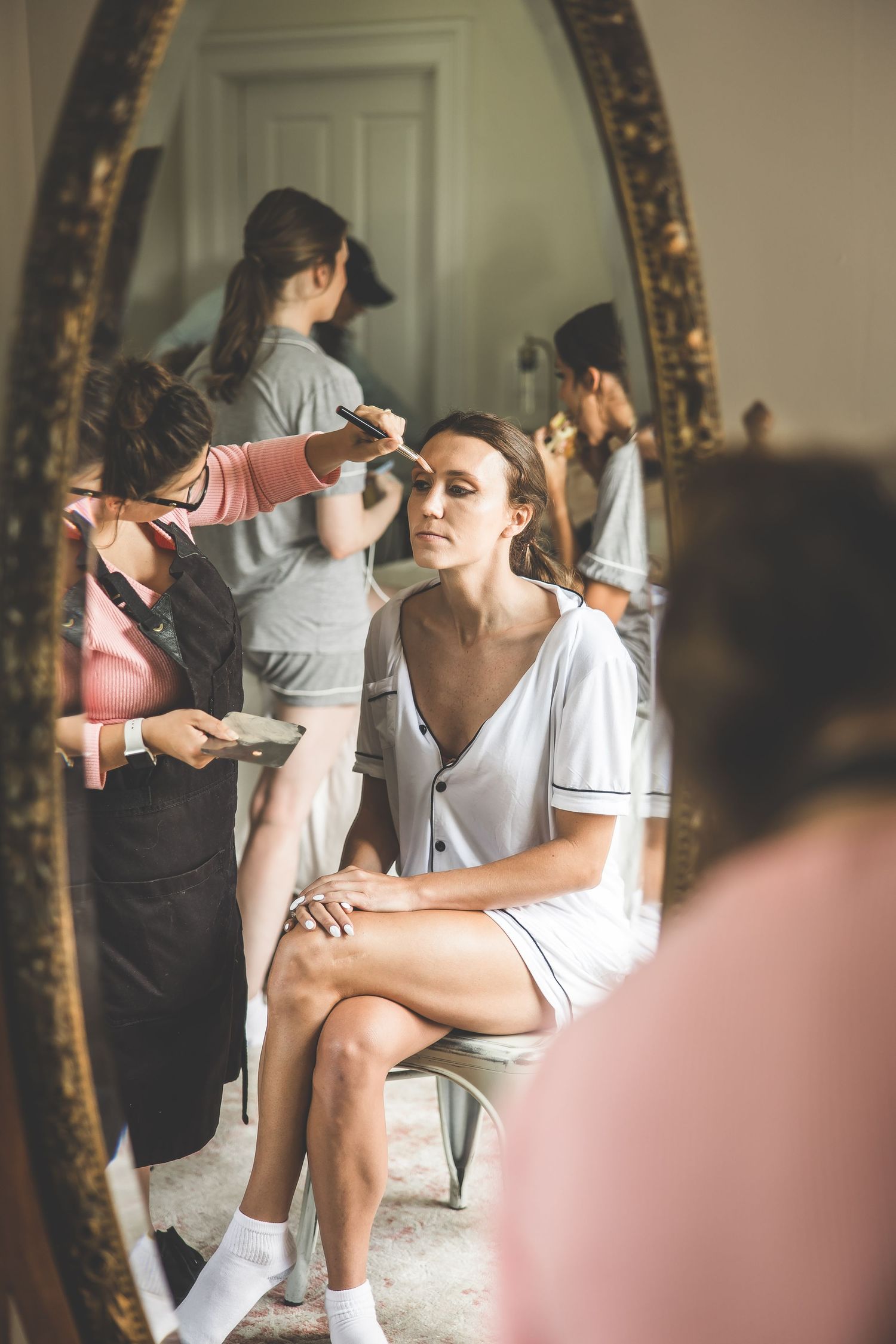 Getting ready scene reflected in ornate gold mirror during wedding preparations.
