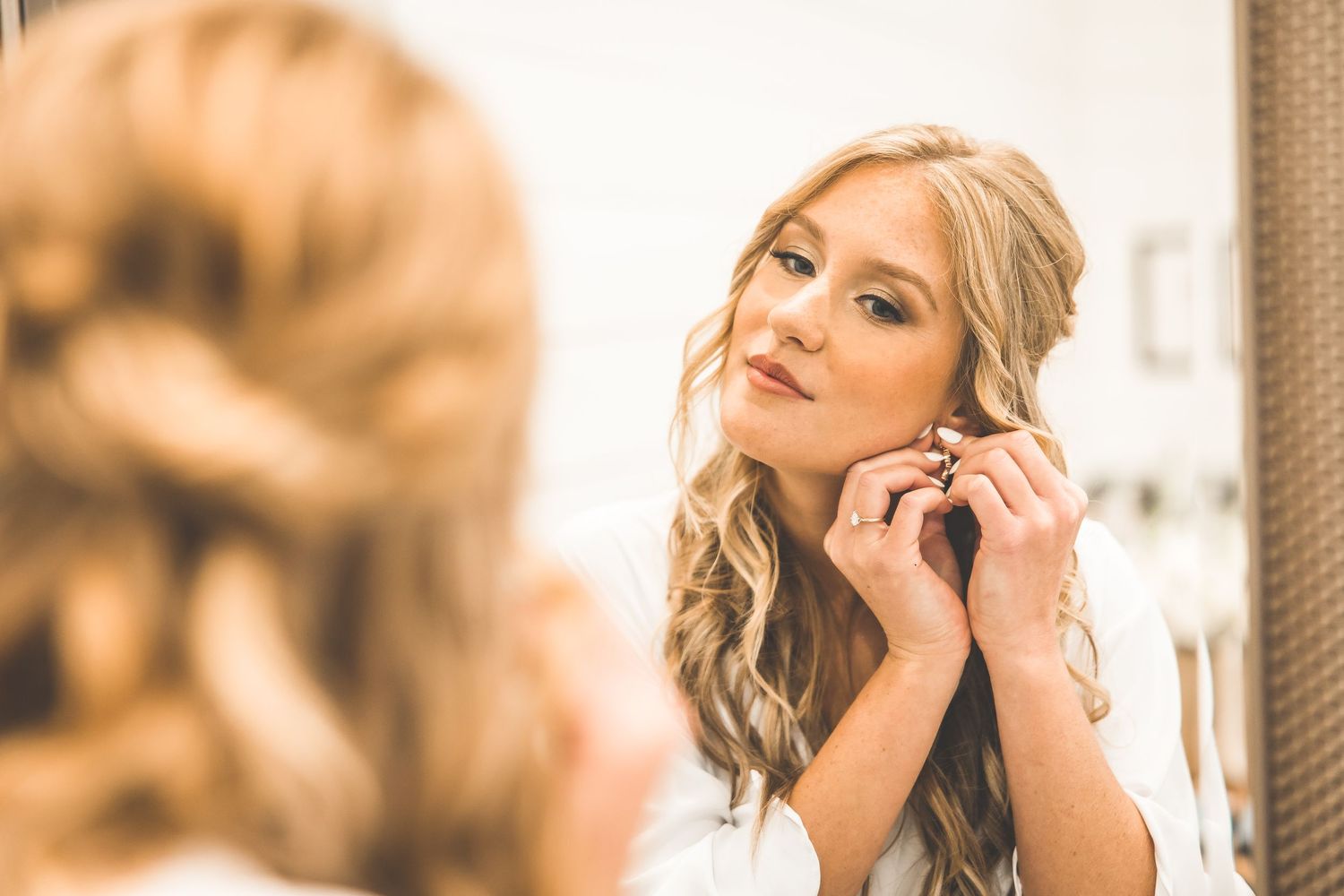 Bride putting on earrings while looking in mirror during wedding preparations.