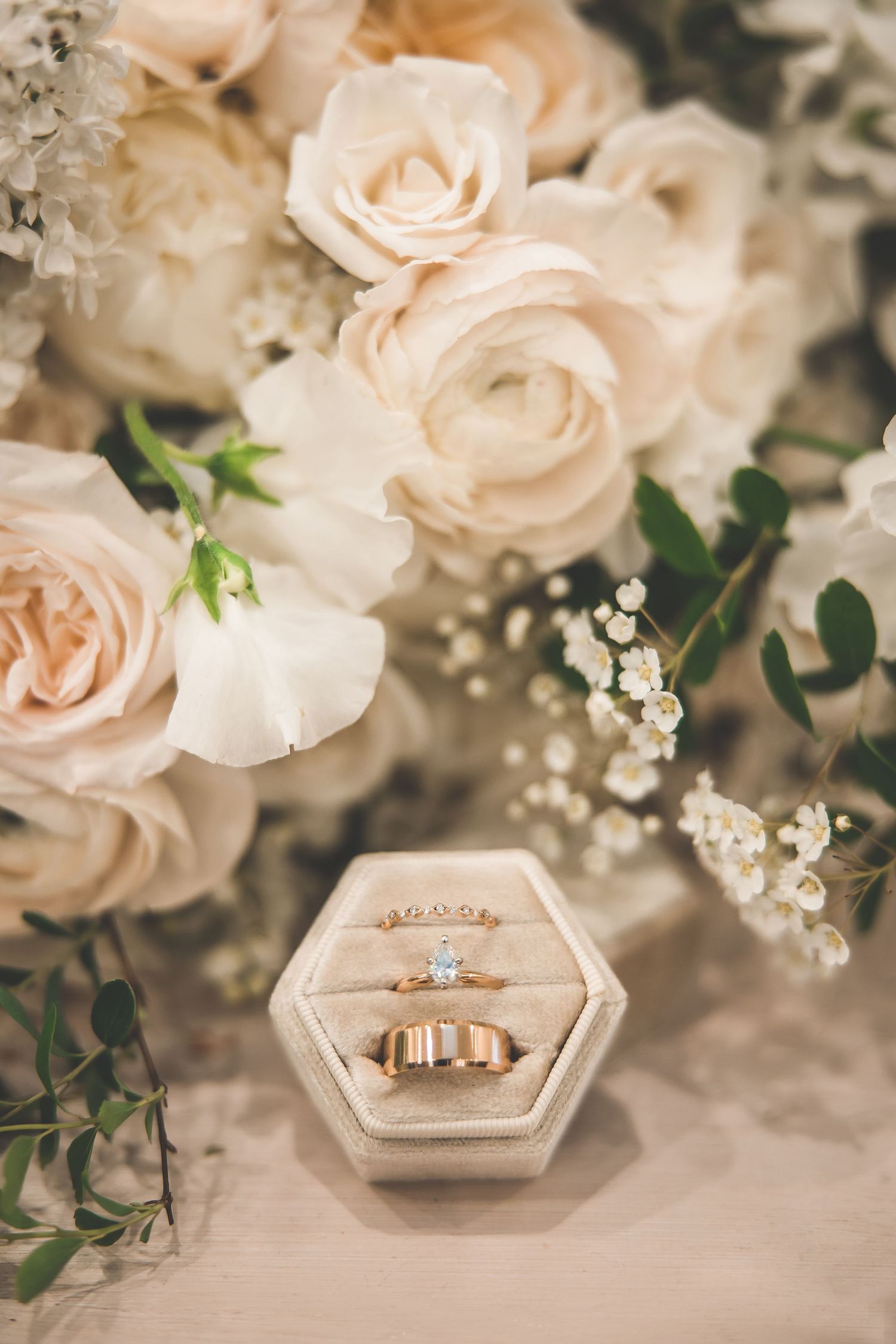 Wedding rings displayed in hexagonal box surrounded by blush roses and baby's breath.
