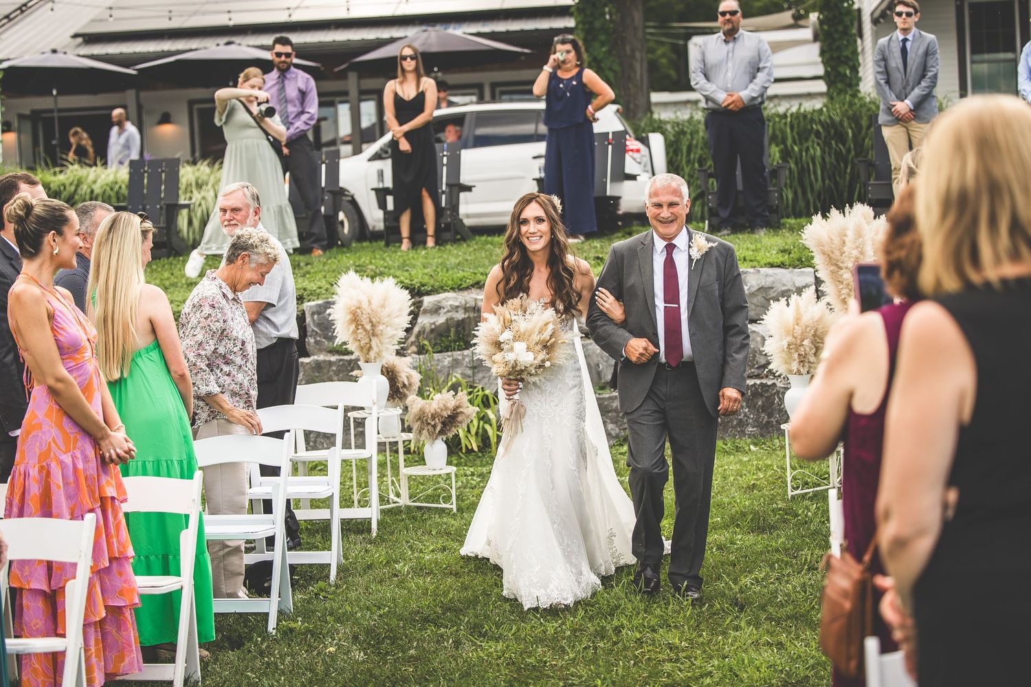 Wedding guests in colorful attire gather on a lawn watching the celebration unfold.
