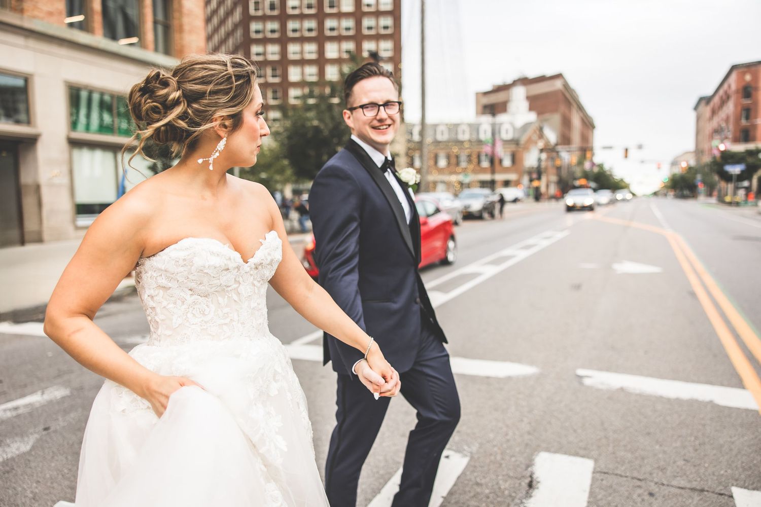 Bride and groom walking together on an urban sidewalk with brick buildings in background.