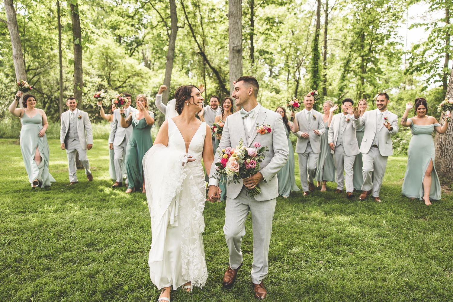 Wedding party celebrates on a grassy lawn with the couple in the center.