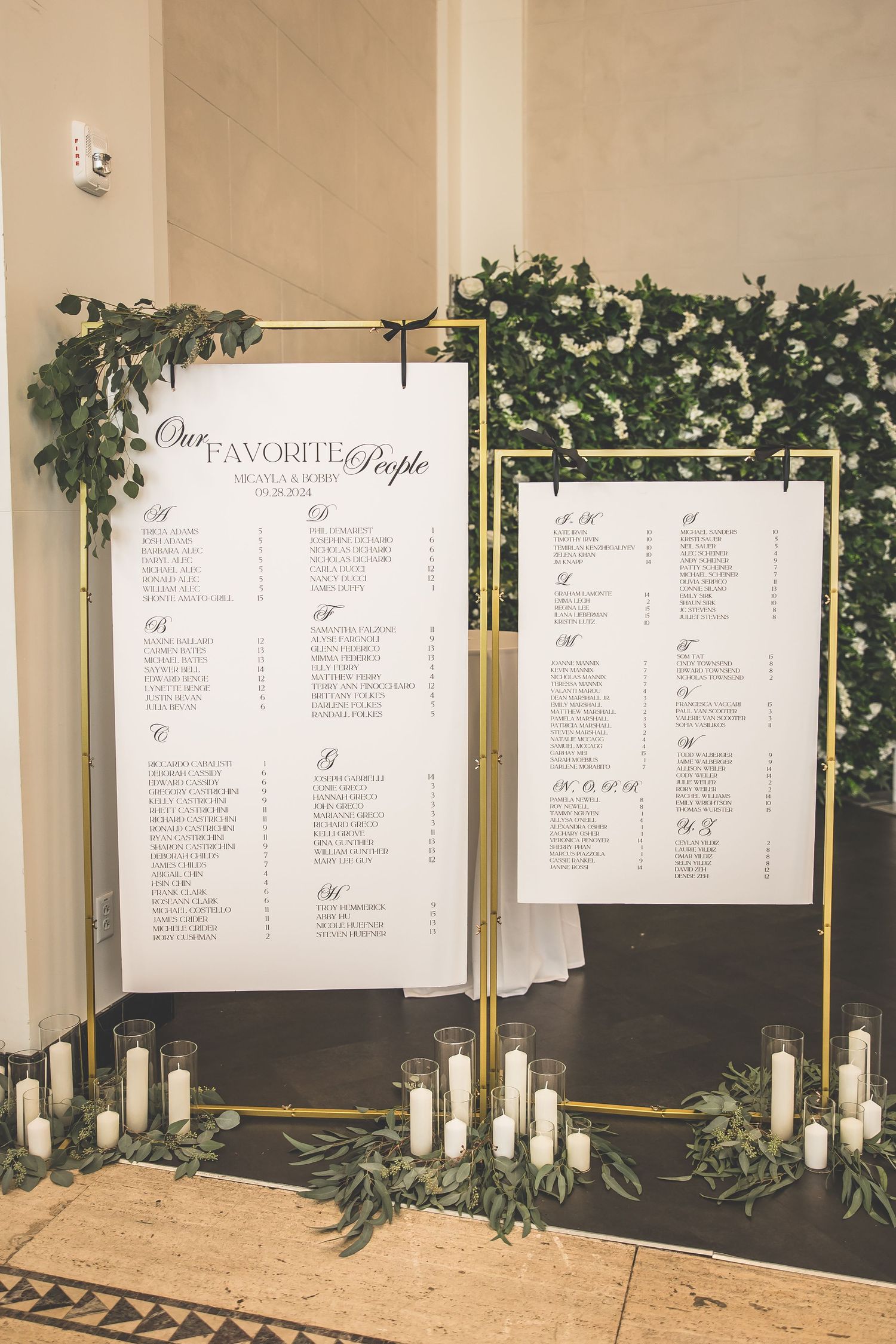 Wedding seating chart display with greenery decorations and candles.