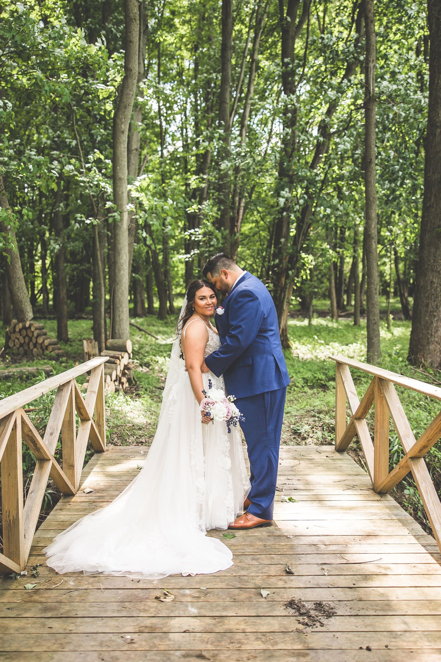 Wedding couple sharing intimate moment on wooden bridge surrounded by lush forest.