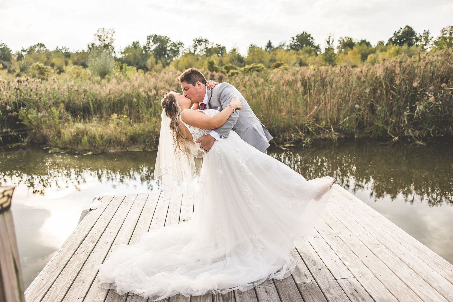A wedding couple shares an intimate moment on a wooden dock surrounded by nature and water.
