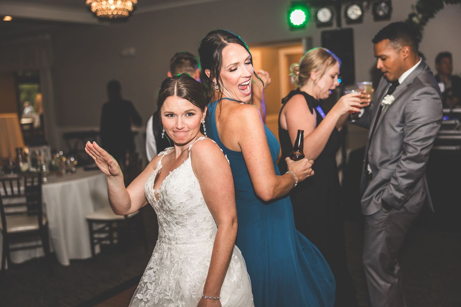 Wedding reception guests dancing and celebrating on dance floor with decorative lighting.