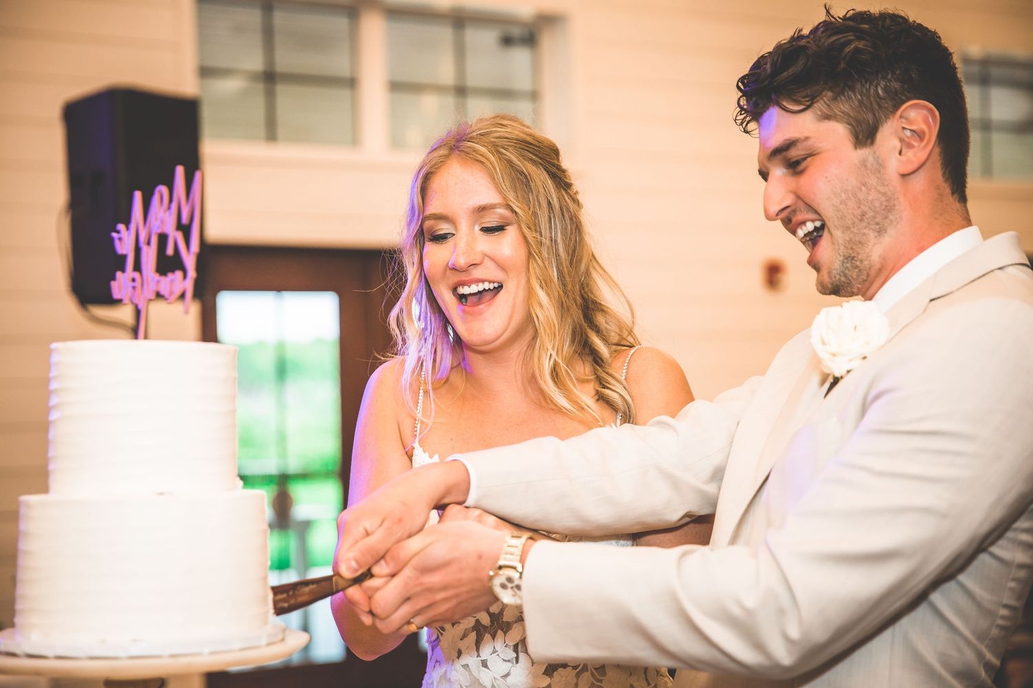 Couple sharing a playful moment while cutting their white wedding cake at reception.