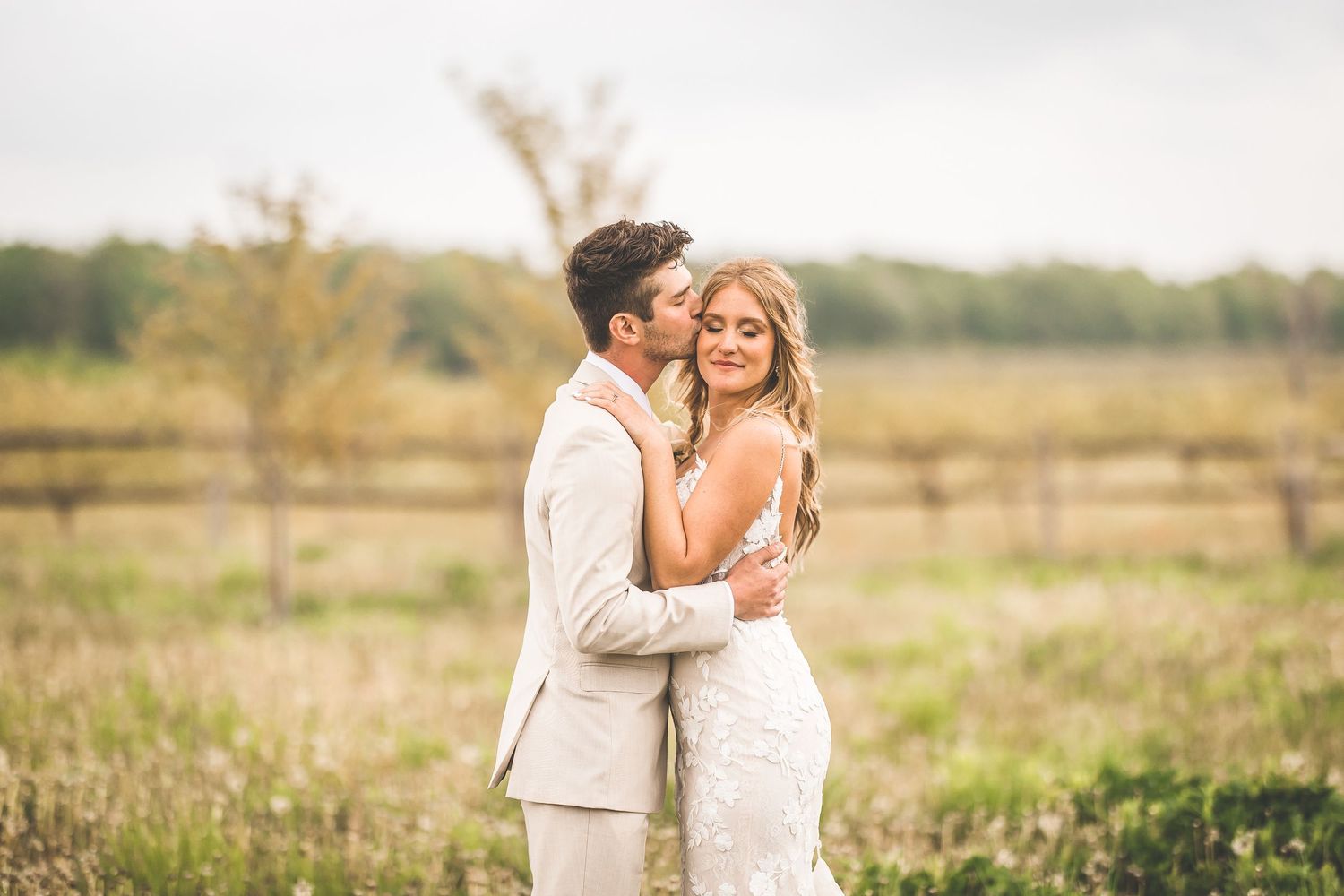 A tender embrace between newlyweds in a golden field during sunset.
