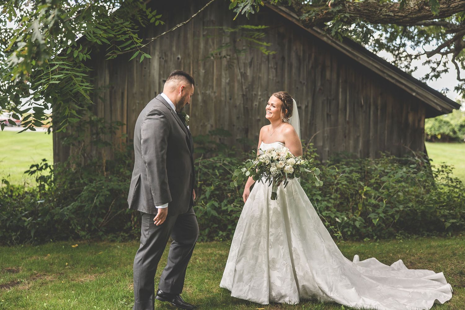 Elegant wedding portraits captured against backdrop of vintage barn and green landscape.