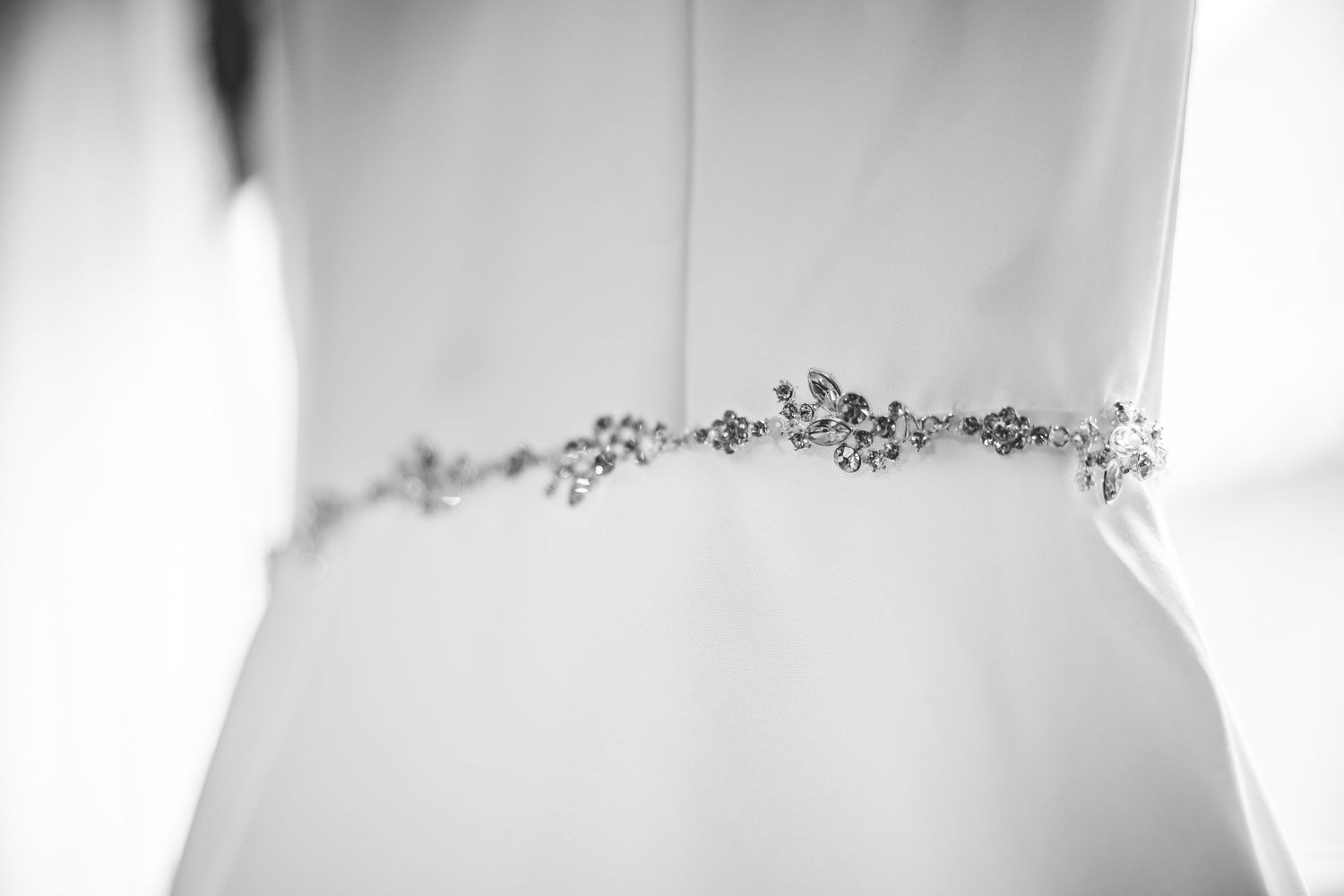 Close-up detail of delicate beaded embellishment on white wedding dress.