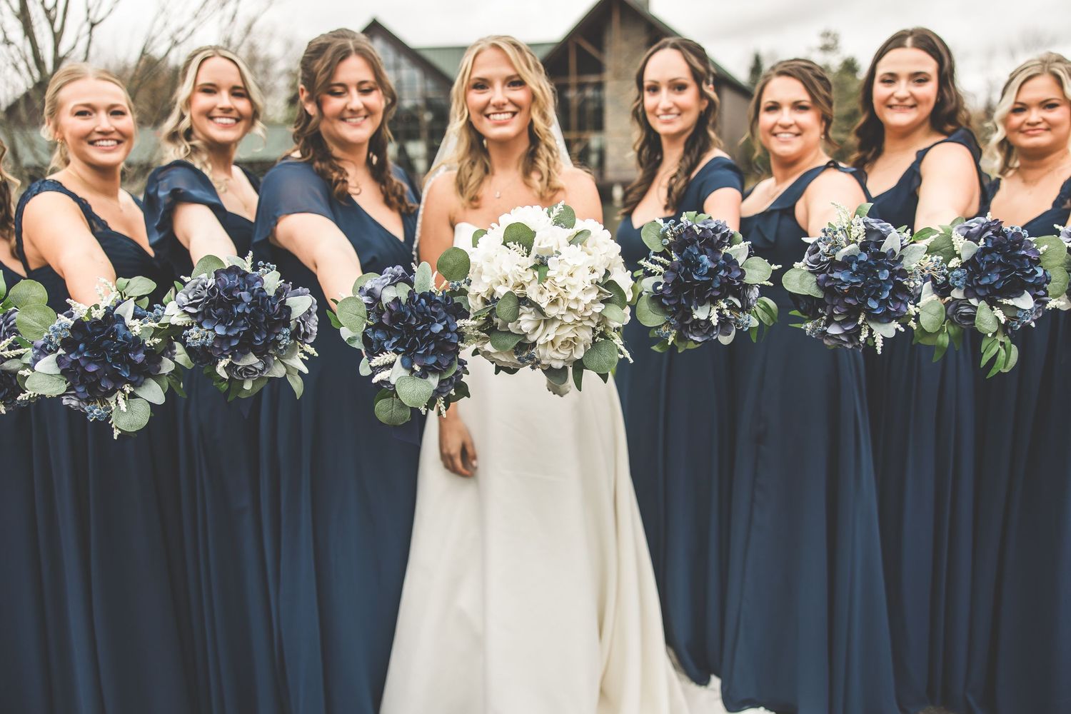 Wedding party in navy blue dresses and white gowns pose together for group photos outdoors.