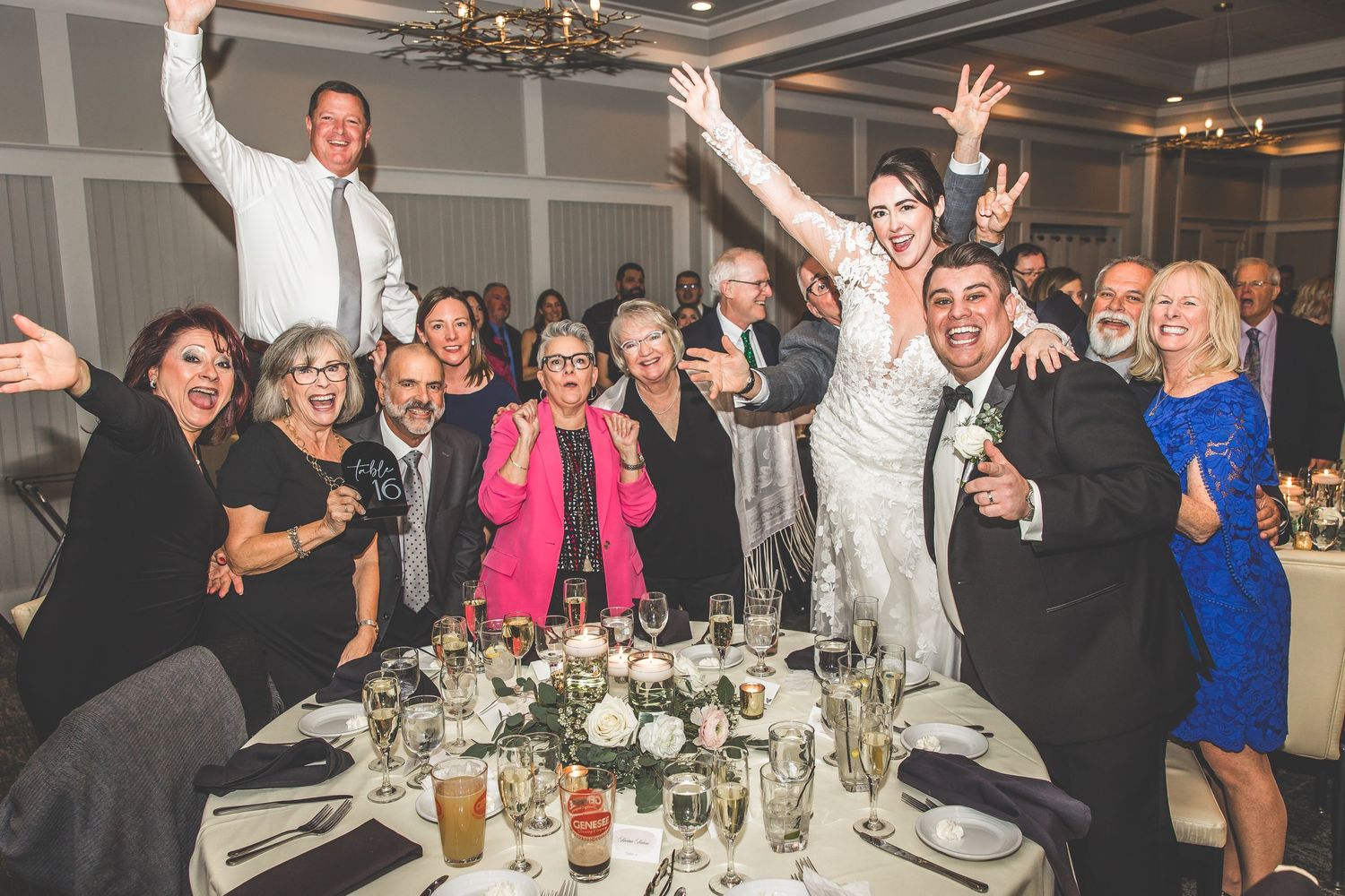 Wedding guests celebrate at reception tables with drinks and lively expressions.