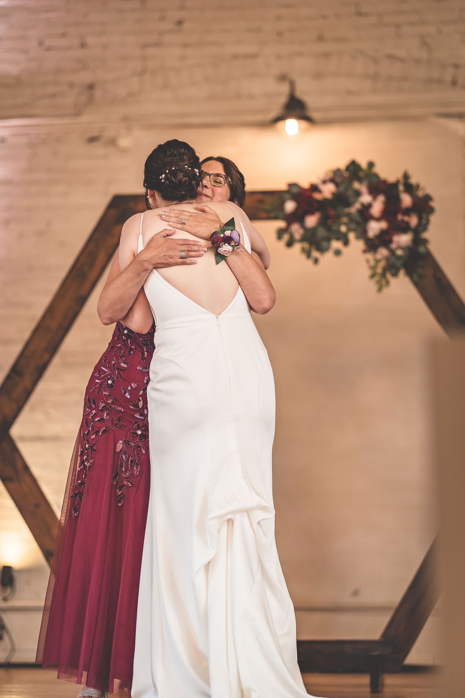 An emotional embrace during a wedding celebration beneath a hexagonal wooden arch.