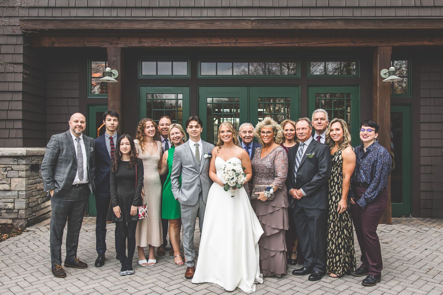 Panoramic shot of wedding party and guests lined up outside a rustic venue building.