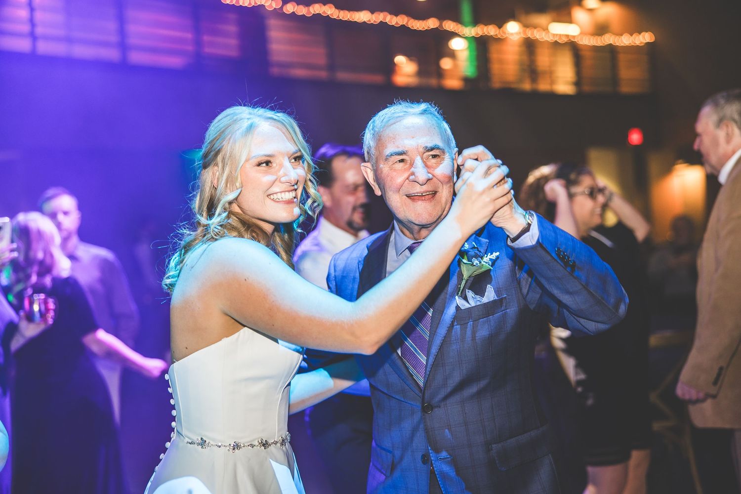 Couples dancing together under dramatic purple and blue lighting at an evening celebration.