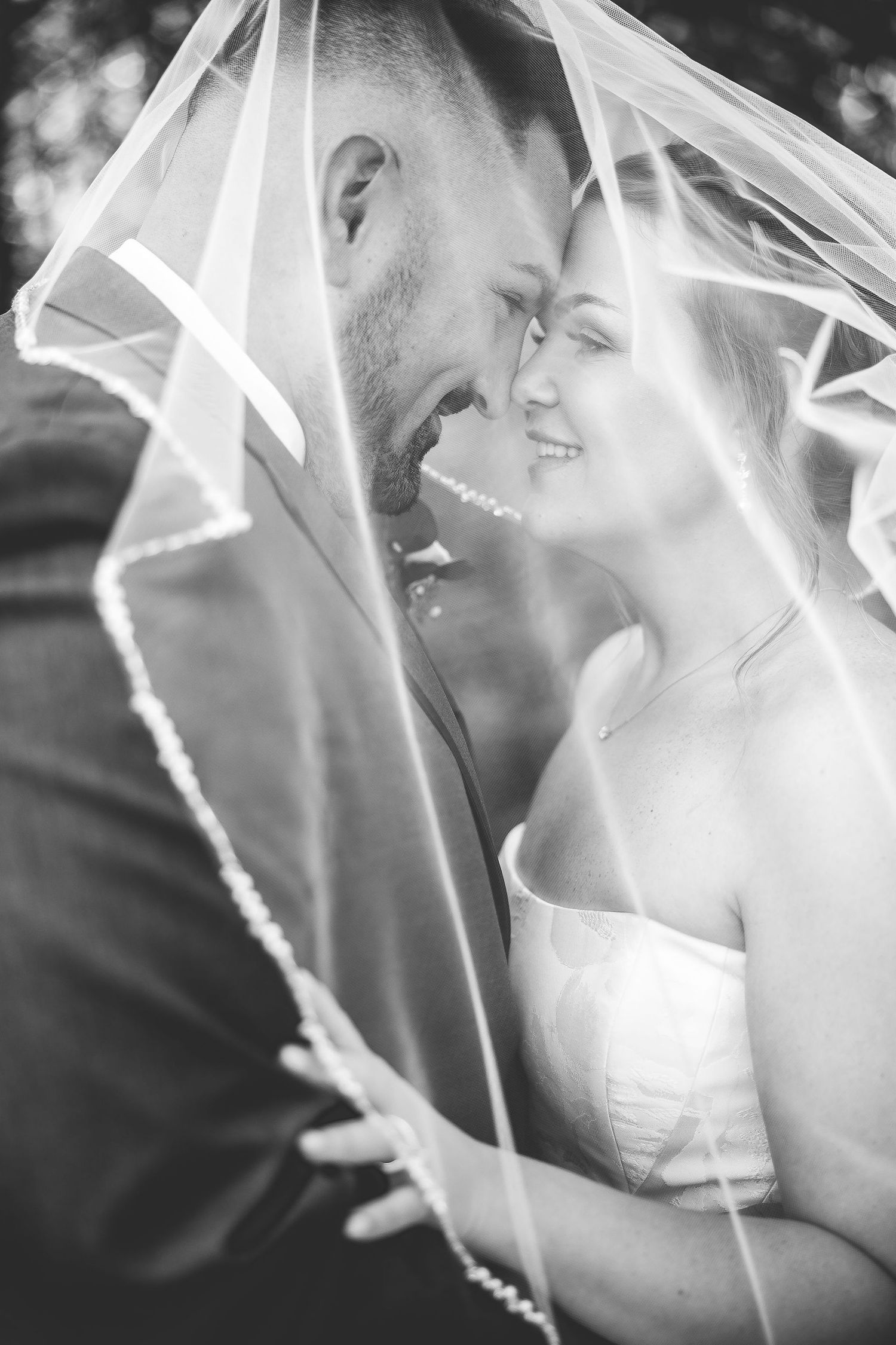 Black and white intimate wedding portrait under delicate veil with natural lighting.