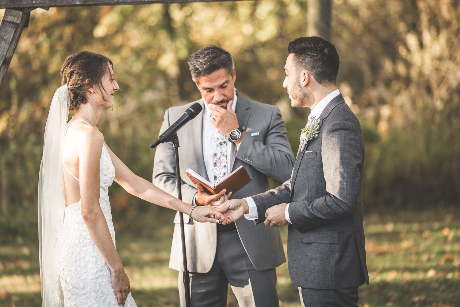 Intimate moment during outdoor wedding ceremony with rustic wooden arch backdrop.