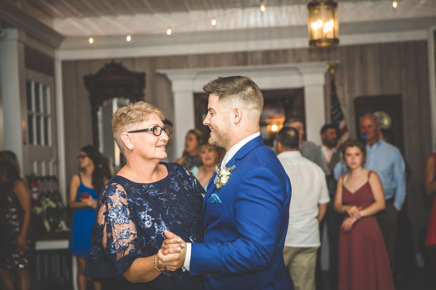 Wedding guests dance and celebrate on a dimly lit dance floor with string lights overhead.