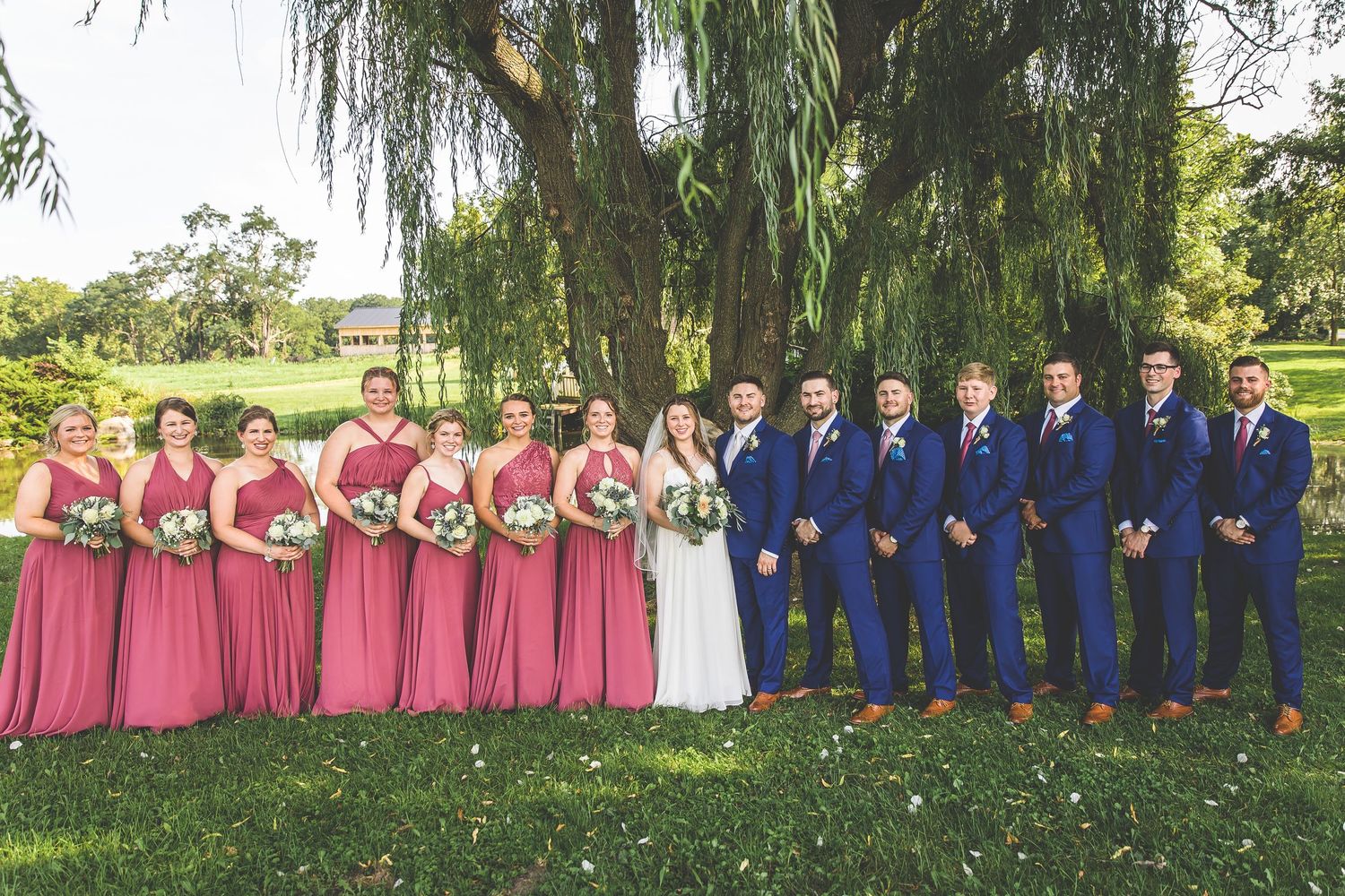 Panoramic wedding party photo under weeping willows with burgundy and navy color scheme.