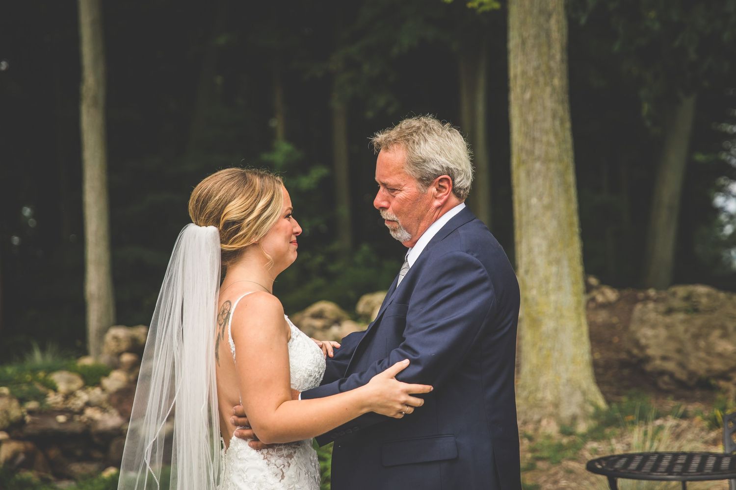 A couple shares an intimate first look moment in a scenic outdoor wedding setting with trees in the background.