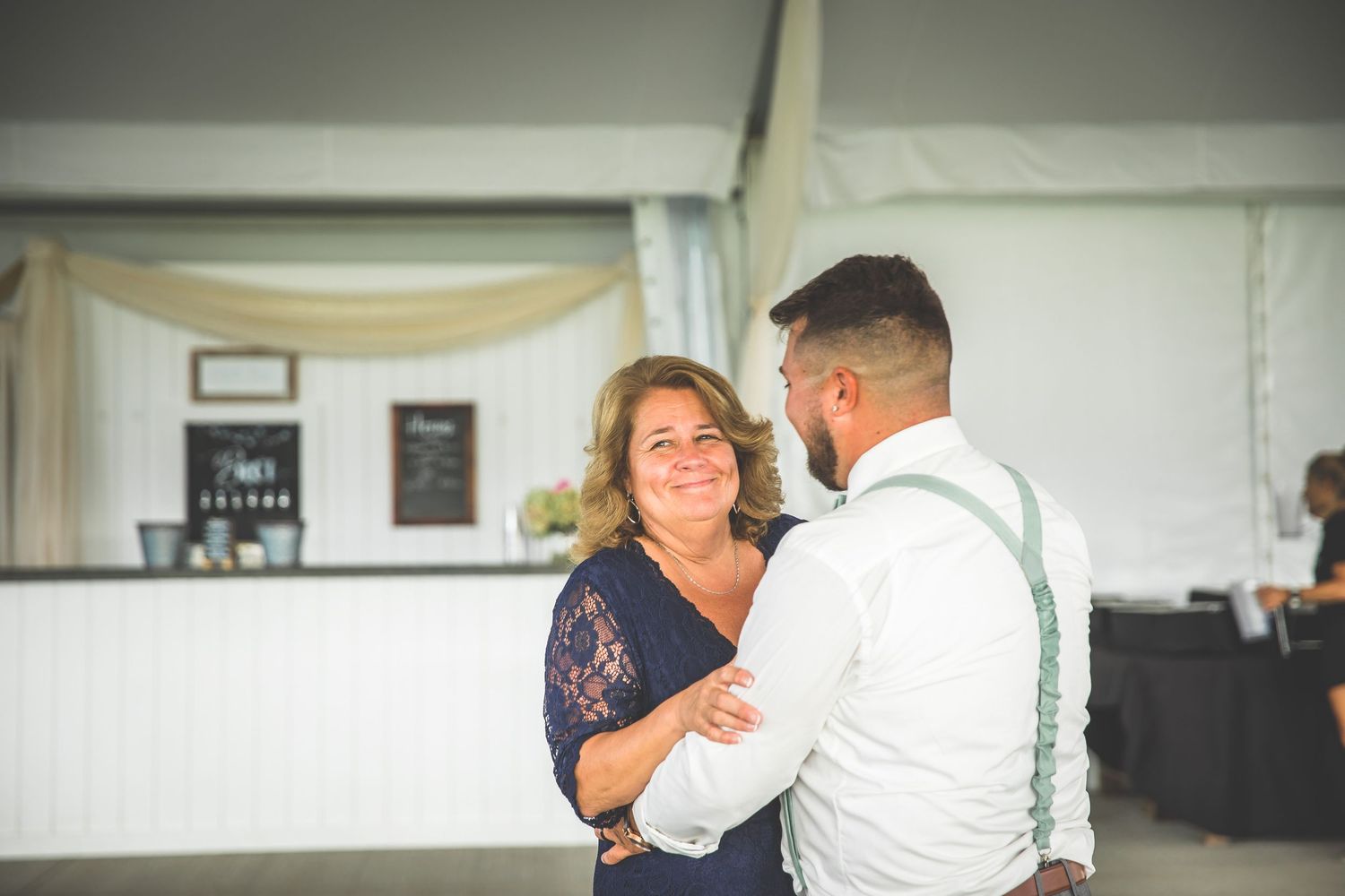 Two people dance together in a sunlit reception venue with white walls and decorative draping.