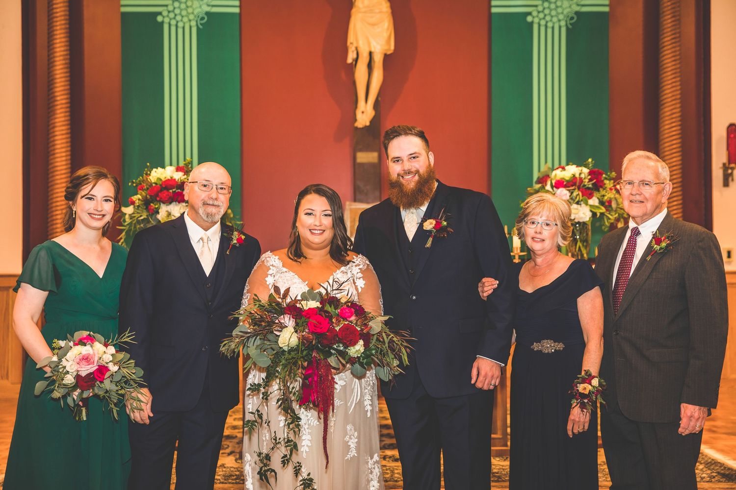 Wedding group photo in church with green columns and religious artwork.