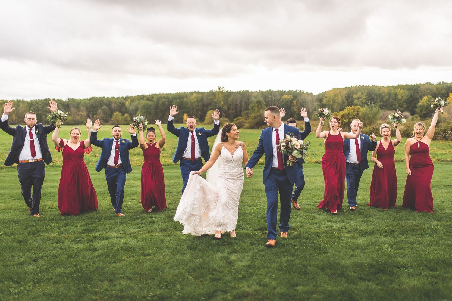 Wedding party arranged in fun poses on green lawn with burgundy and navy color coordination.