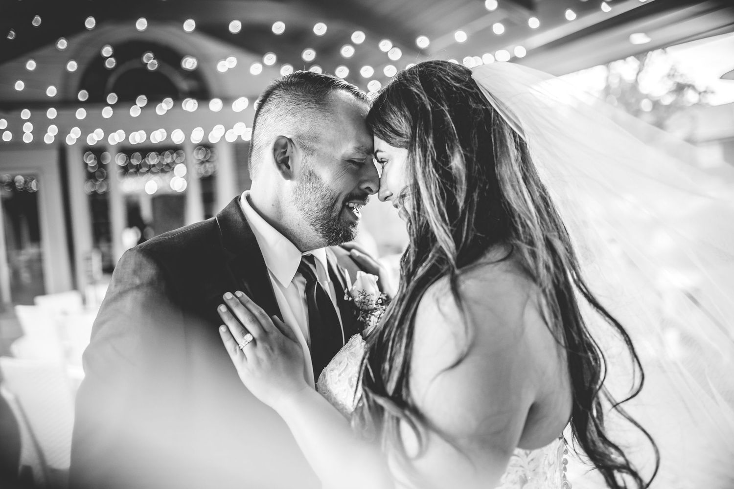 Romantic black and white portrait of newlyweds sharing an intimate moment under string lights.