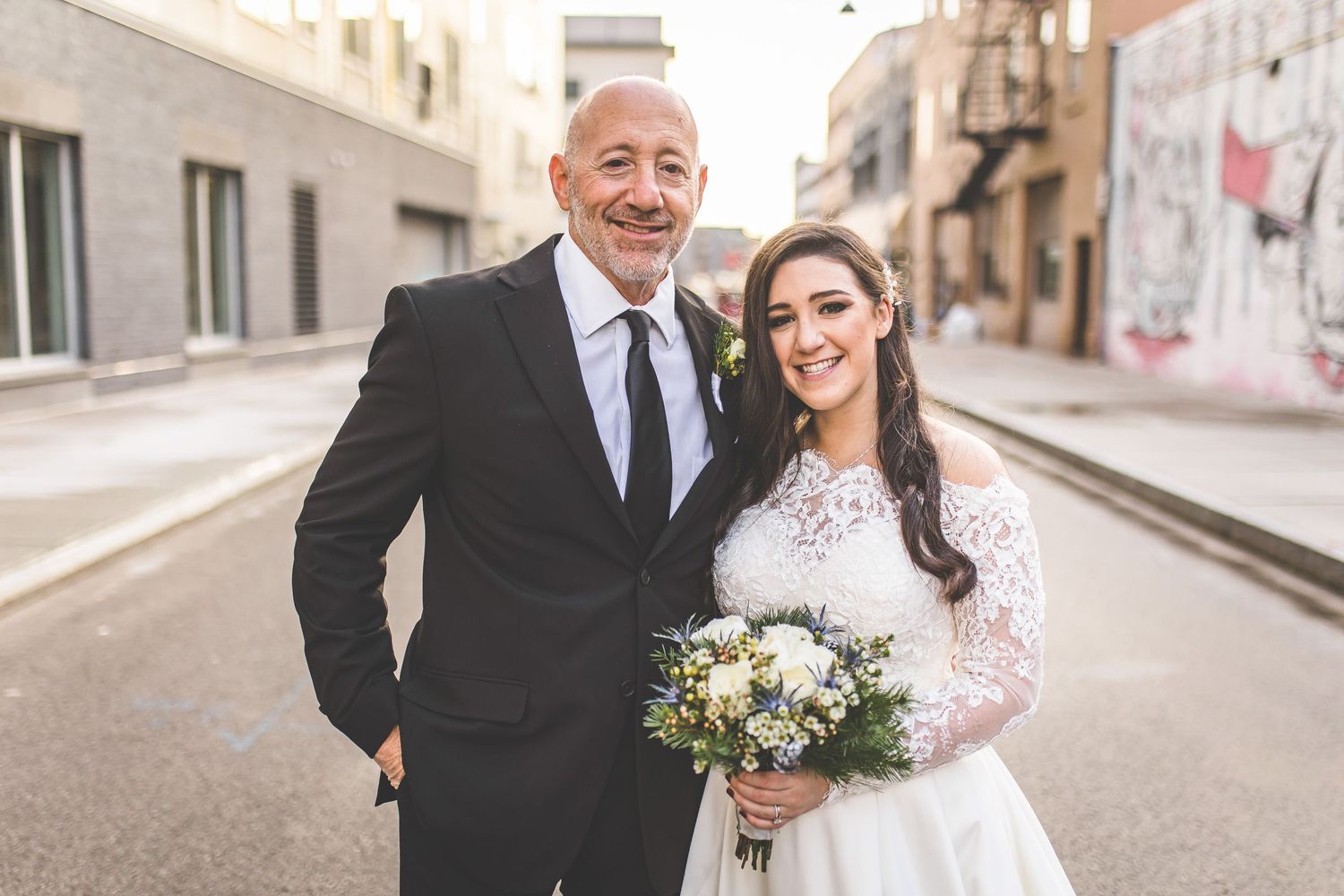 Wedding party members smile and laugh together on urban sidewalk.
