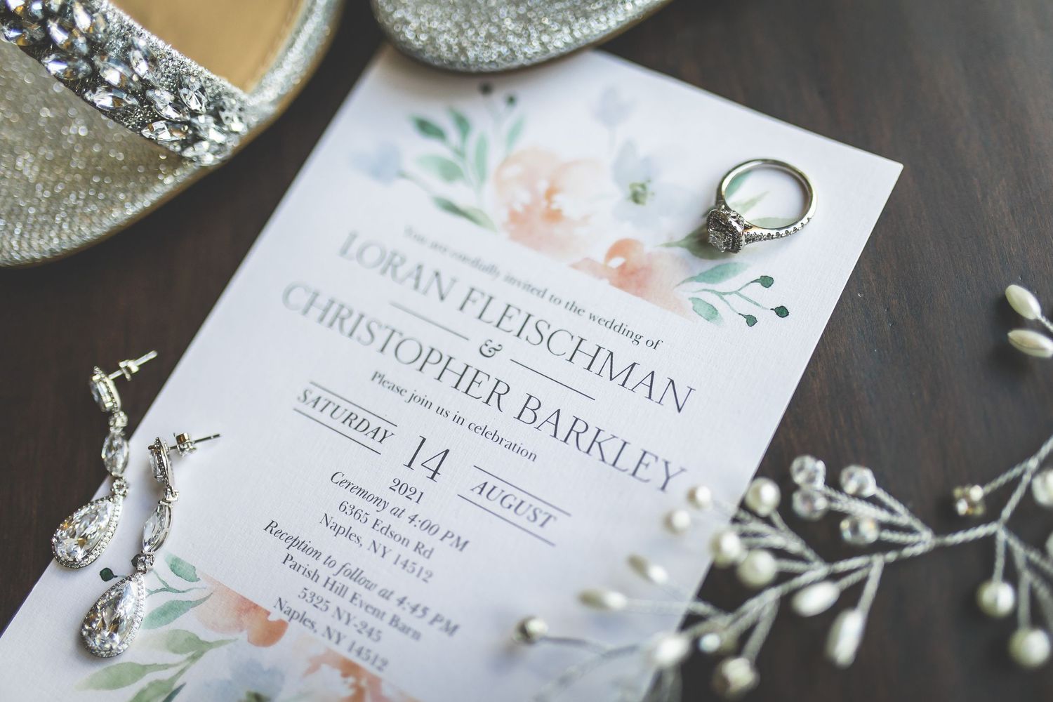 Elegant floral wedding invitations with watercolor details and rings displayed on dark surface.