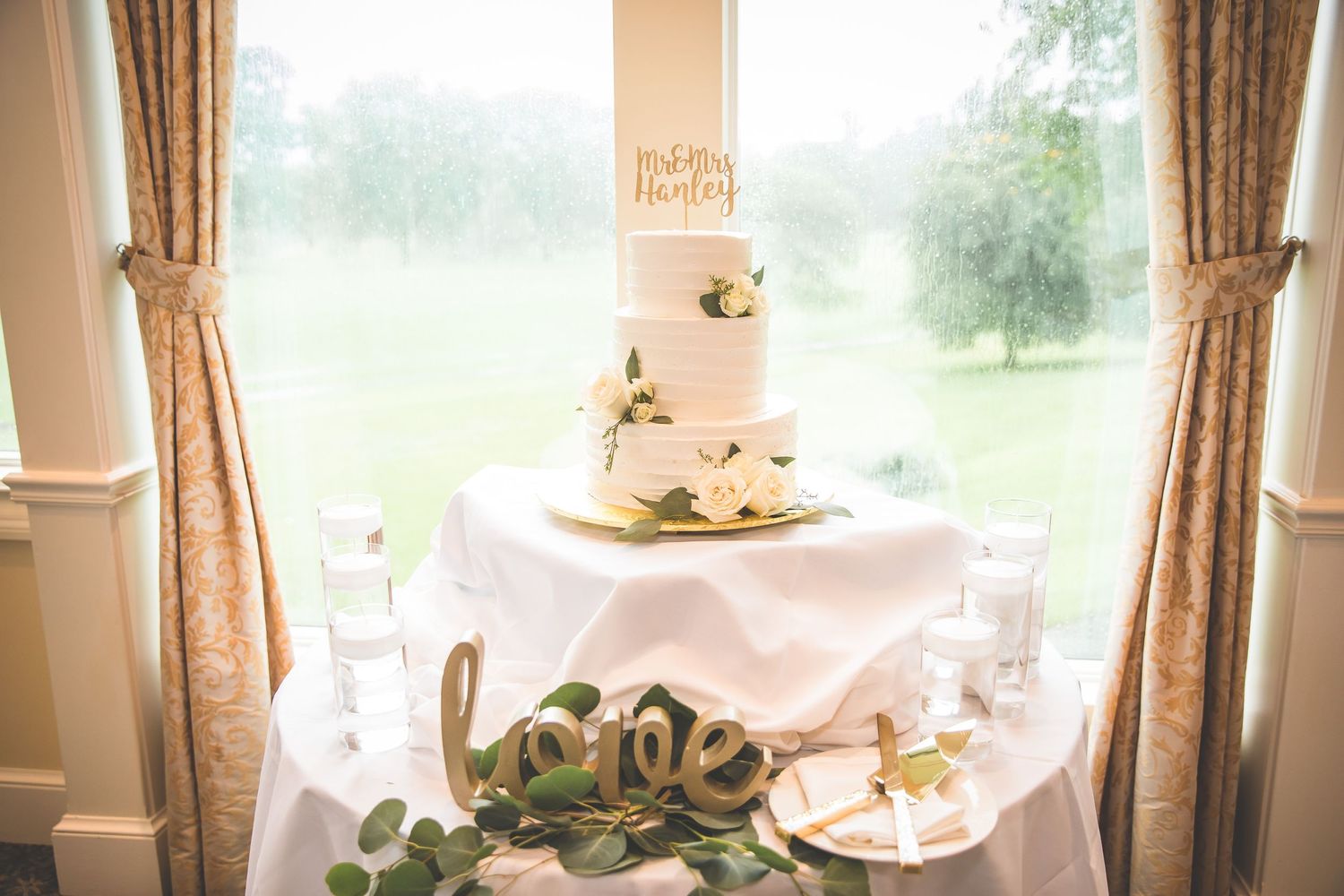 Wedding reception venue with natural light streaming through draped windows.