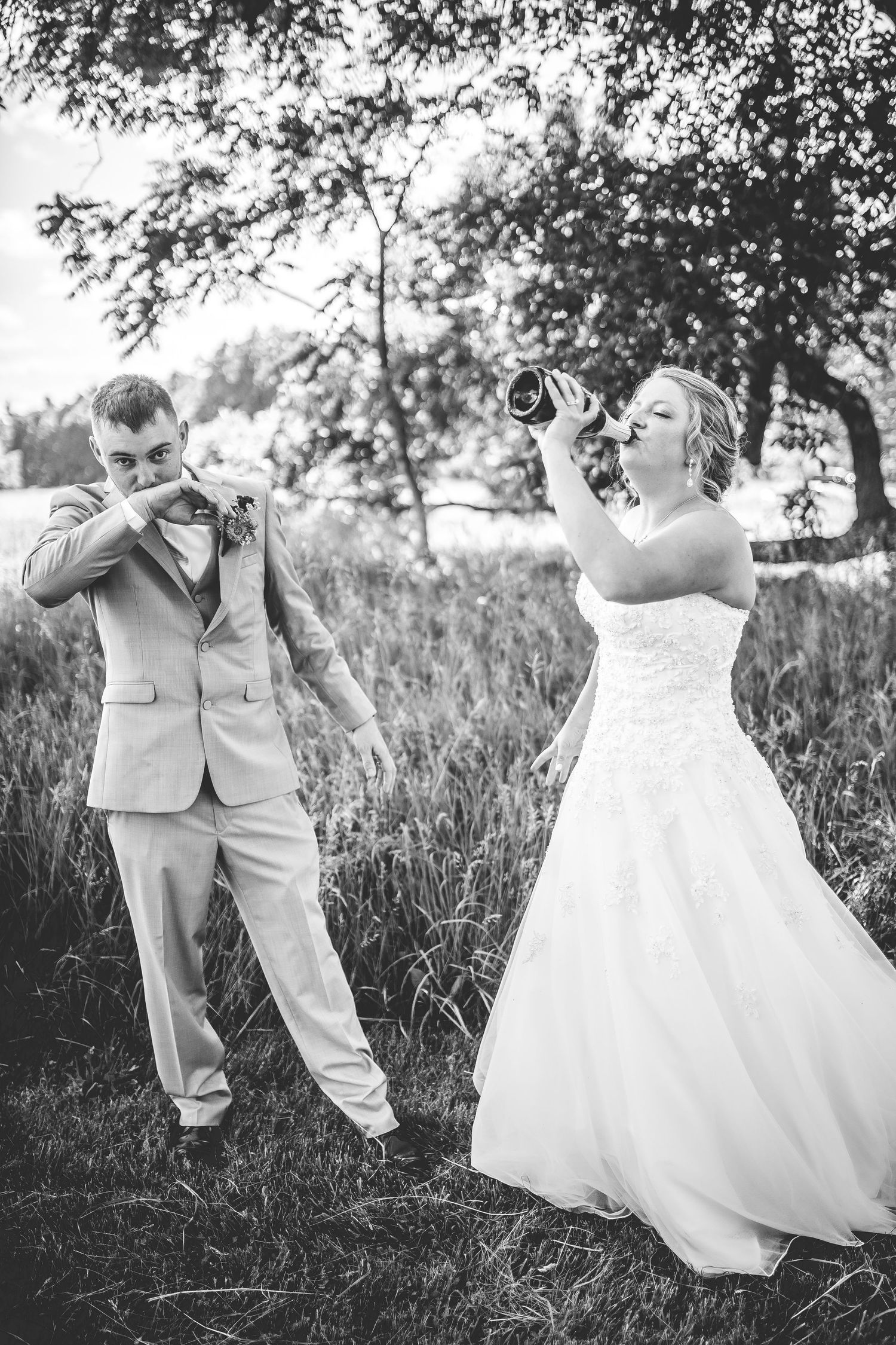 Wedding couple playfully drinks from bottles in black and white garden portrait.