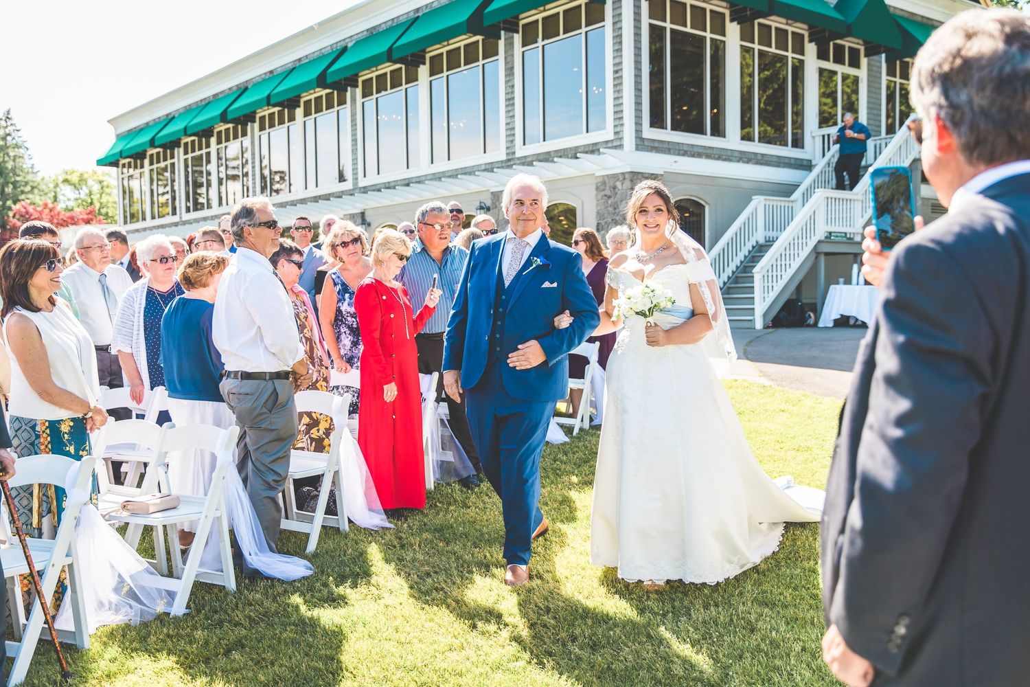 Outdoor wedding reception setup with white chairs and tents on a sunny afternoon.