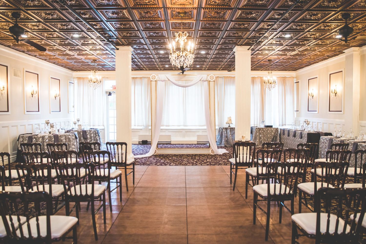 Elegant wedding venue with ornate ceiling, crystal chandeliers and rows of dark chairs.