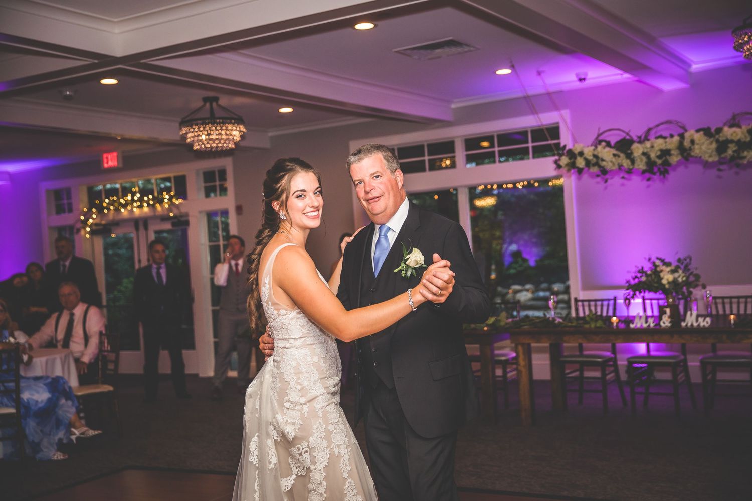 Wedding reception venue decorated with purple uplighting and elegant chandeliers.