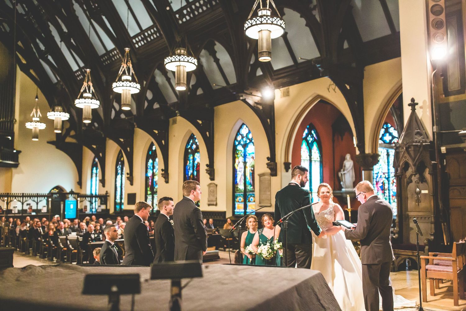 Wide angle shot of a church wedding ceremony with dramatic lighting and stained glass windows.