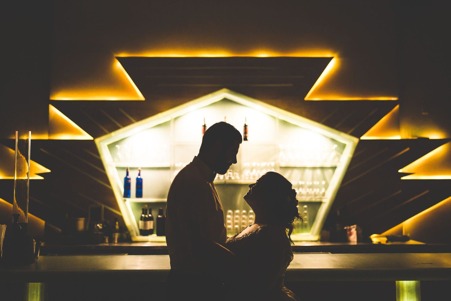 Silhouetted figures at a dimly lit bar with dramatic golden lighting creating an atmospheric ambiance.