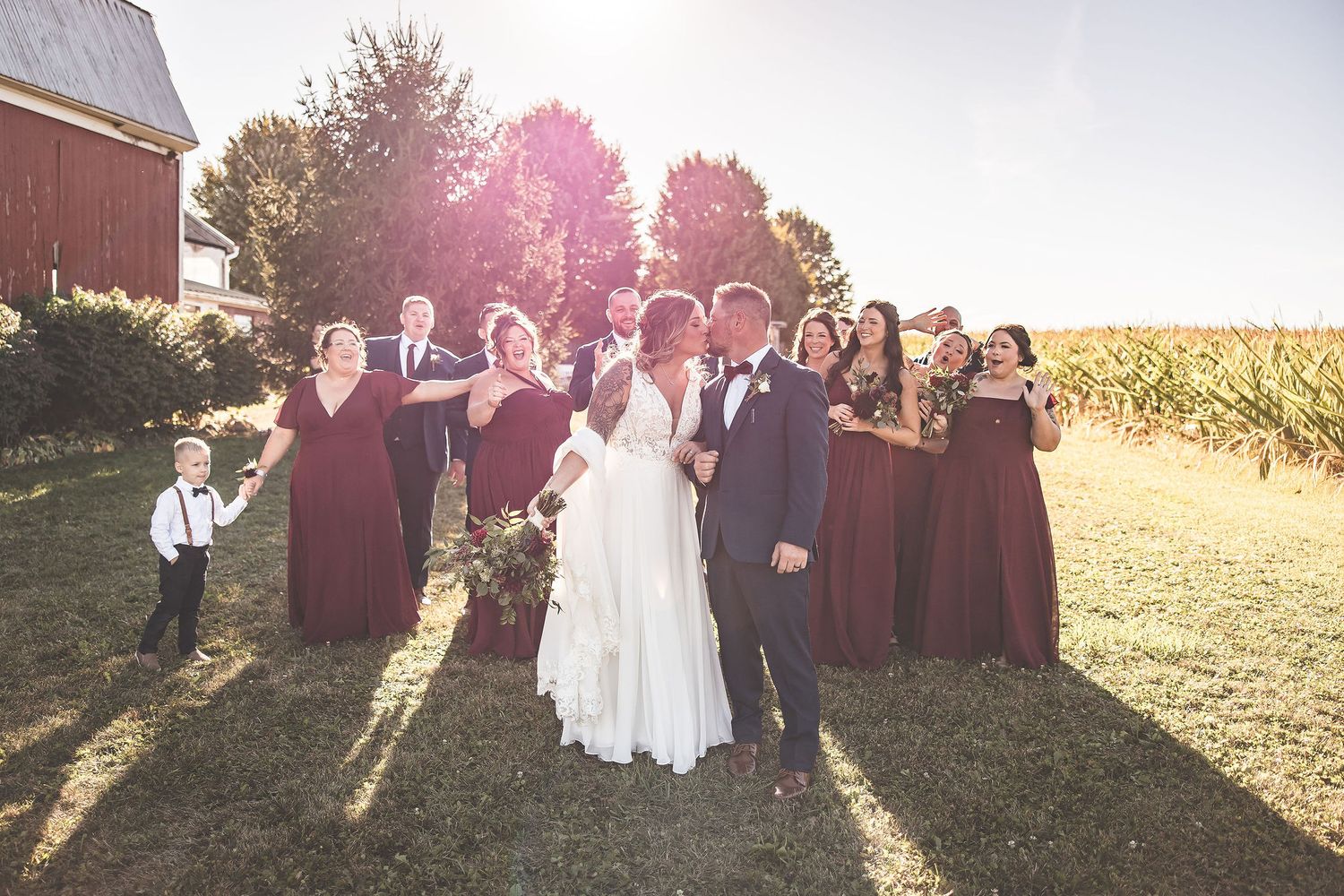 Golden hour wedding party photos with sun flare against rustic farm backdrop.