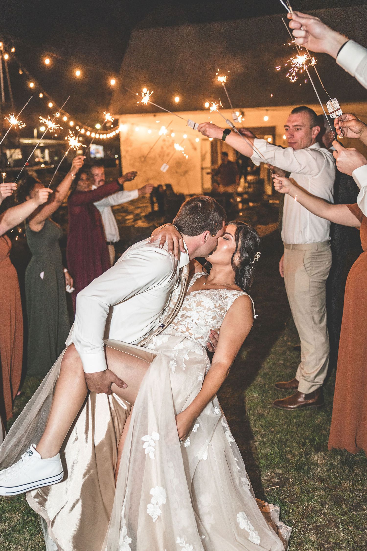 Wedding guests form a sparkler tunnel for the newlyweds during an outdoor evening celebration.
