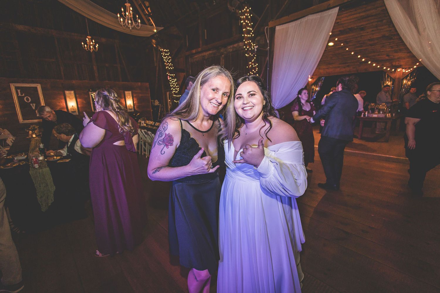 Wedding party dancing and celebrating in a dimly lit rustic venue with purple uplighting.