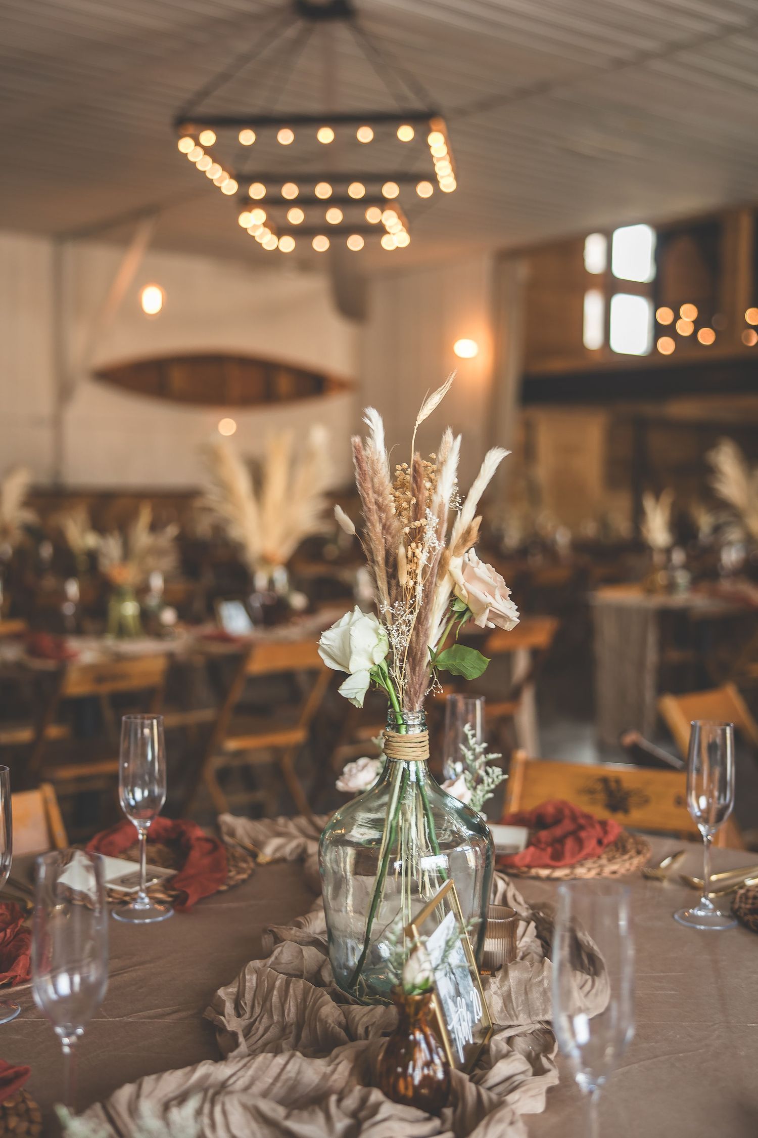 Rustic wedding table settings with dried floral arrangements and wine glasses under ambient lighting.