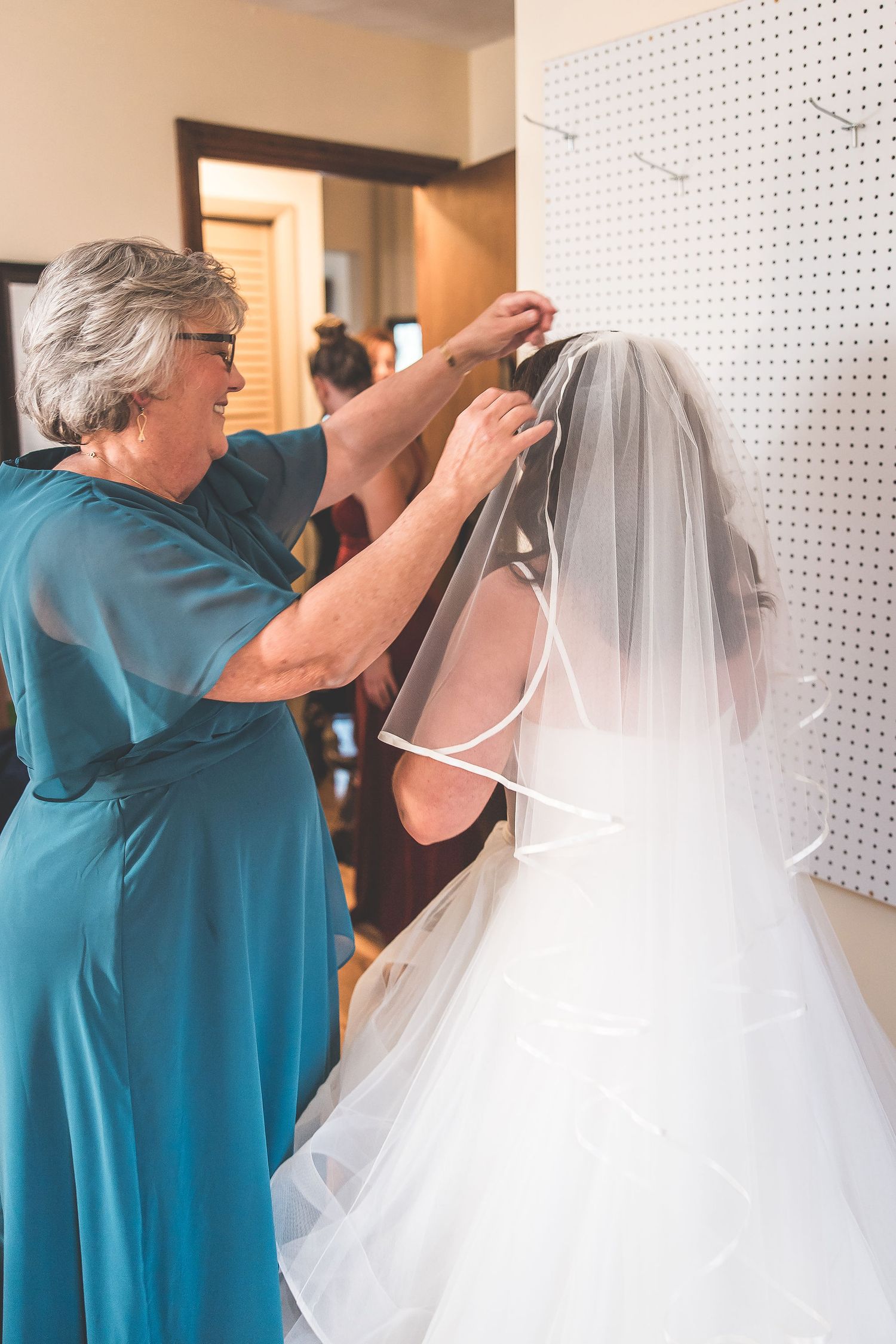 Someone helps adjust a wedding veil on a bride wearing a white dress.