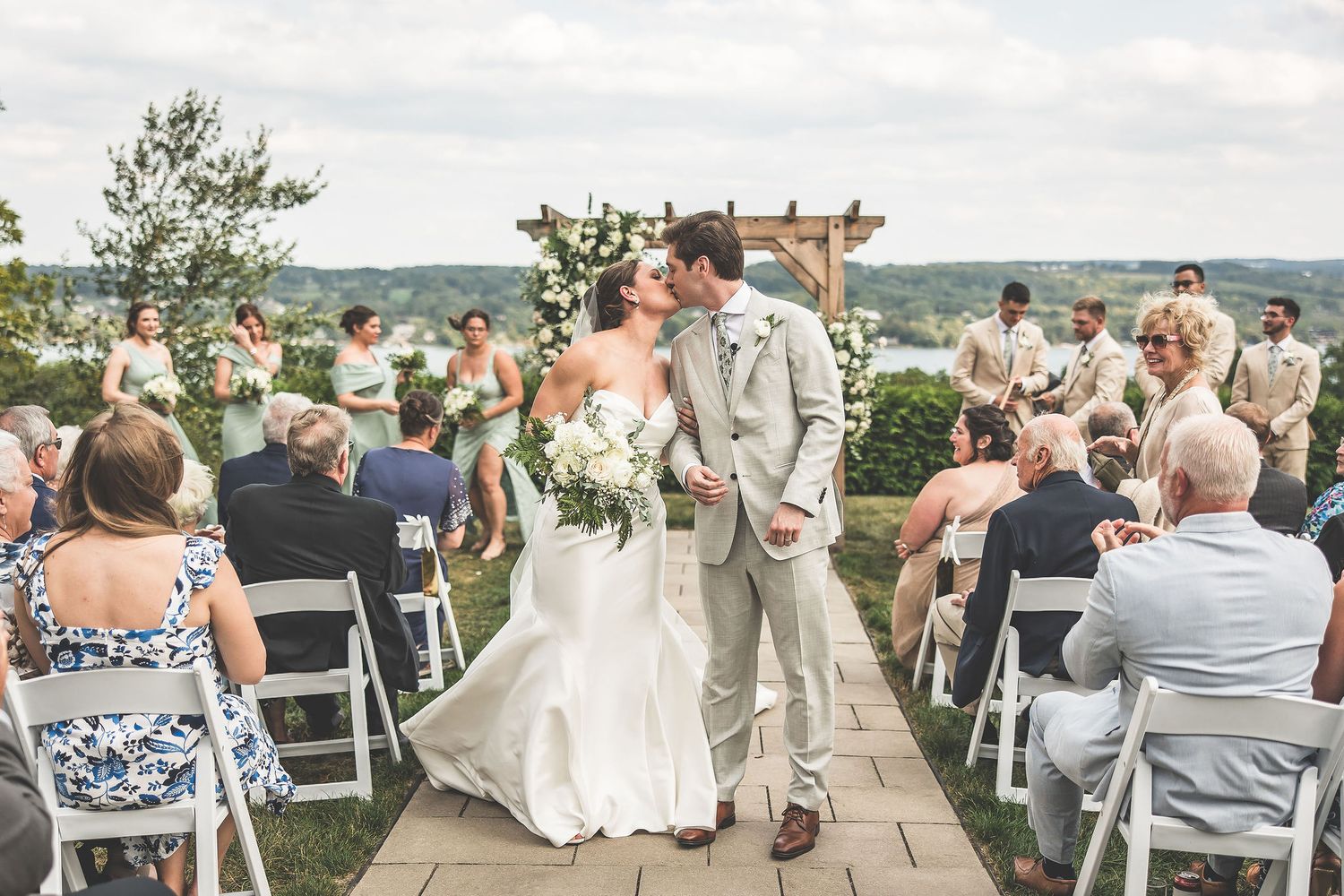 Newlyweds walk down aisle after outdoor ceremony under wooden pergola with scenic view.