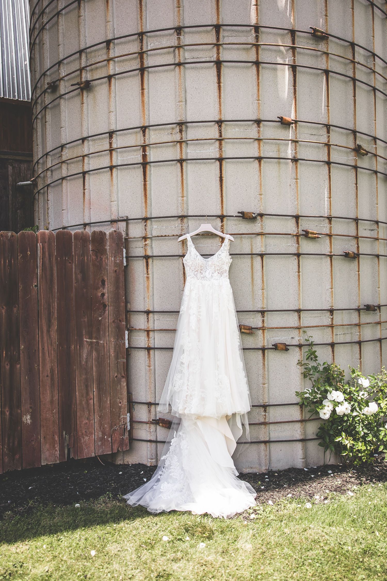 A white wedding dress and flower girl dress displayed against an industrial metal wall outdoors.
