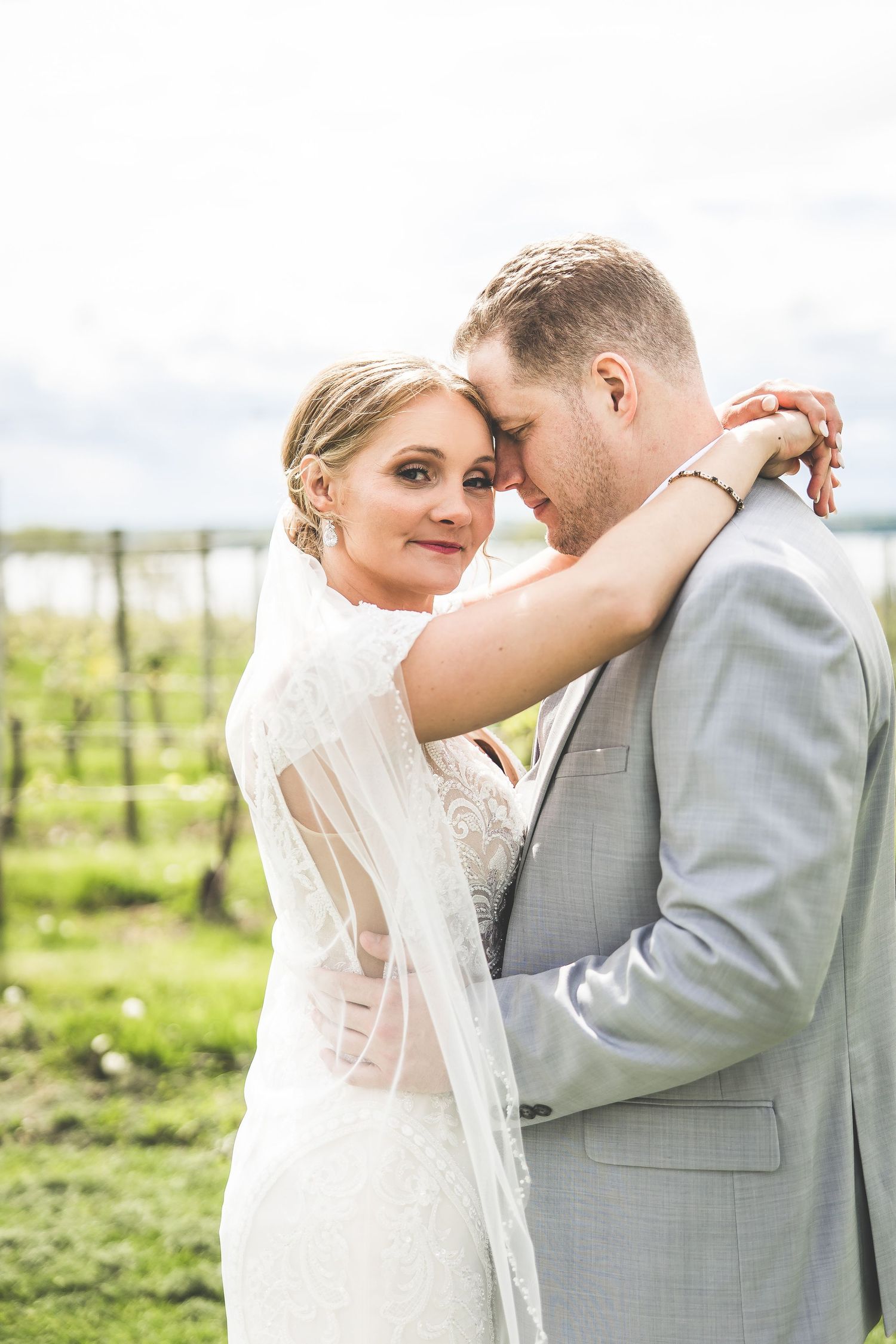 Romantic wedding couple embracing in an intimate moment against a vineyard backdrop.