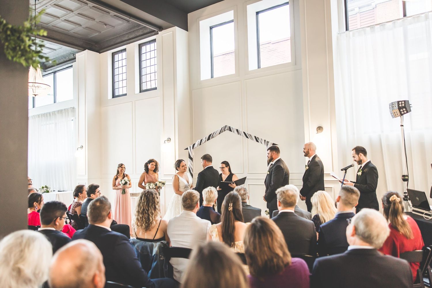 Wide view of wedding ceremony space showing guests seated in rows with natural light streaming in.